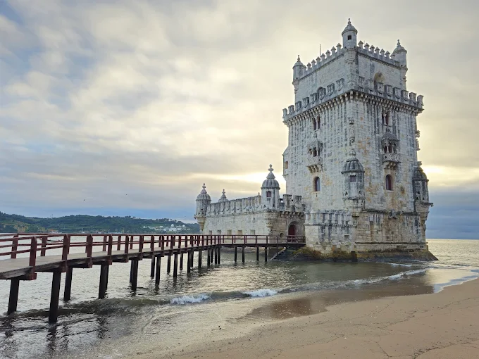 Belém Tower Lisbon at golden hour with Manueline stone fortress rising from Tagus River waters against warm sunset sky