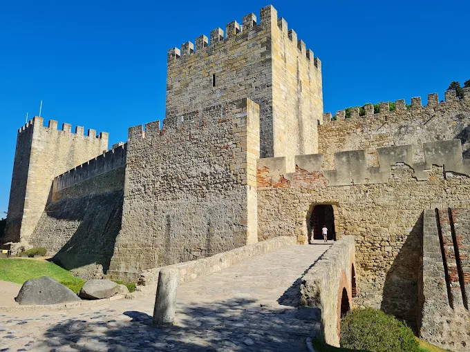 Golden hour sunlight illuminating the ancient stone walls of São Jorge Castle overlooking Lisbon's red rooftops.