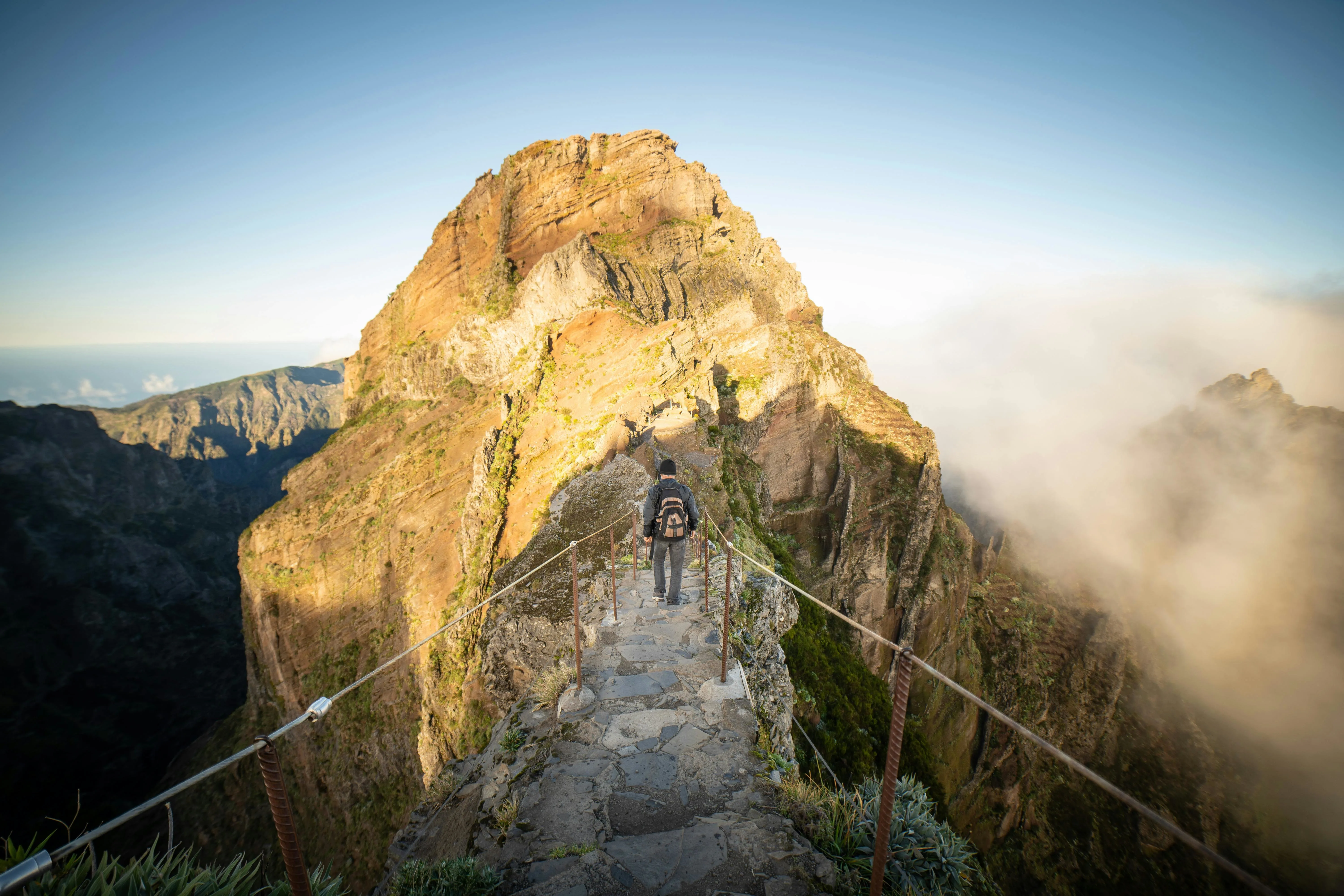 Golden sunrise illuminating Pico do Arieiro's rocky summit above sea of clouds in Madeira's mountainous landscape at dawn