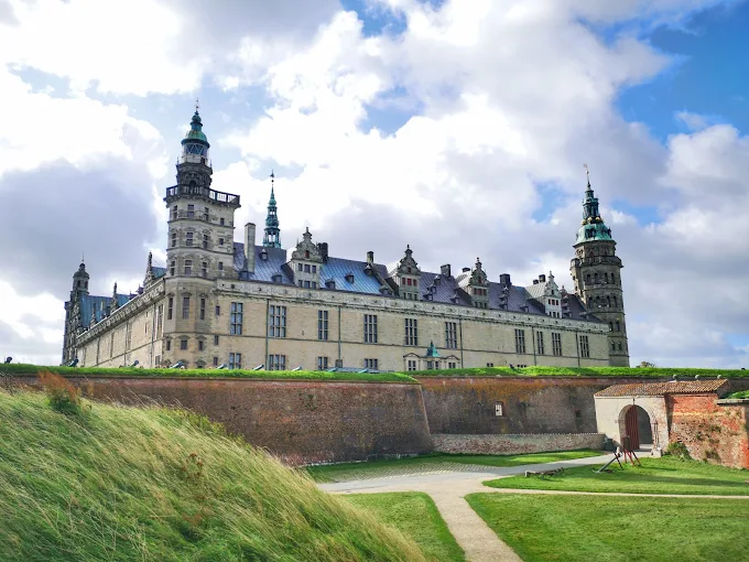 Kronborg Castle Renaissance architecture at sunset with Øresund Strait waters reflecting golden light and medieval towers silhouetted against dramatic sky