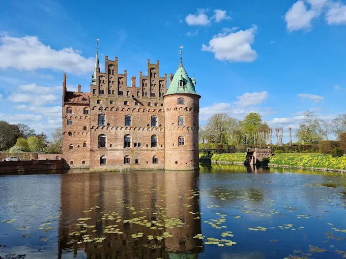 Egeskov Castle Renaissance water castle with red brick towers reflected in moat waters at golden hour on Funen Denmark