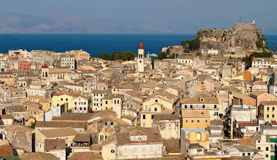 Pastel Venetian buildings reflecting on morning canal waters in Corfu Old Town, Greece.