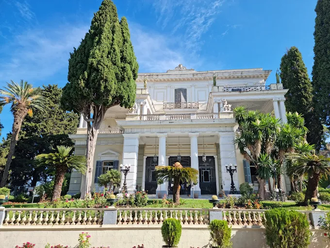 Sunlight illuminating the neoclassical Achilleion Palace statues and terraces overlooking the Ionian Sea.