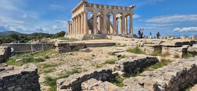 Aegina Temple of Aphaia at golden hour, Greece: Ancient Doric columns against Saronic Gulf backdrop, soft evening light illuminating marble ruins with distant islands visible