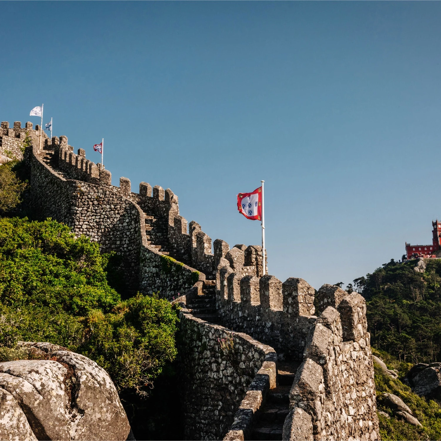Morning mist parting around the ancient granite battlements of the Moorish Castle in Sintra, Portugal.