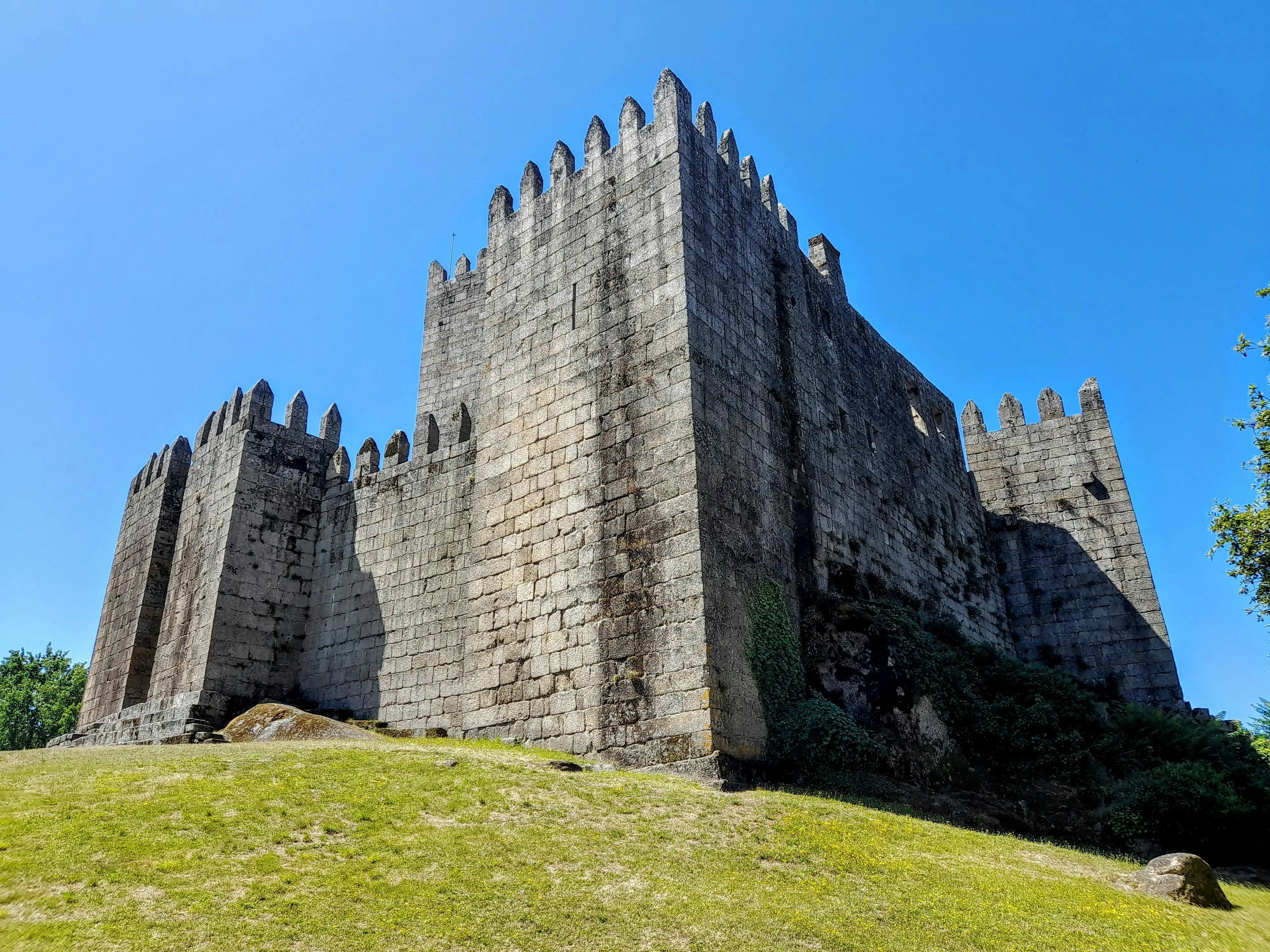 Guimarães Castle at golden hour, Portugal: Medieval stone fortress overlooking historic city, soft evening light illuminating 10th-century walls where Portugal was born