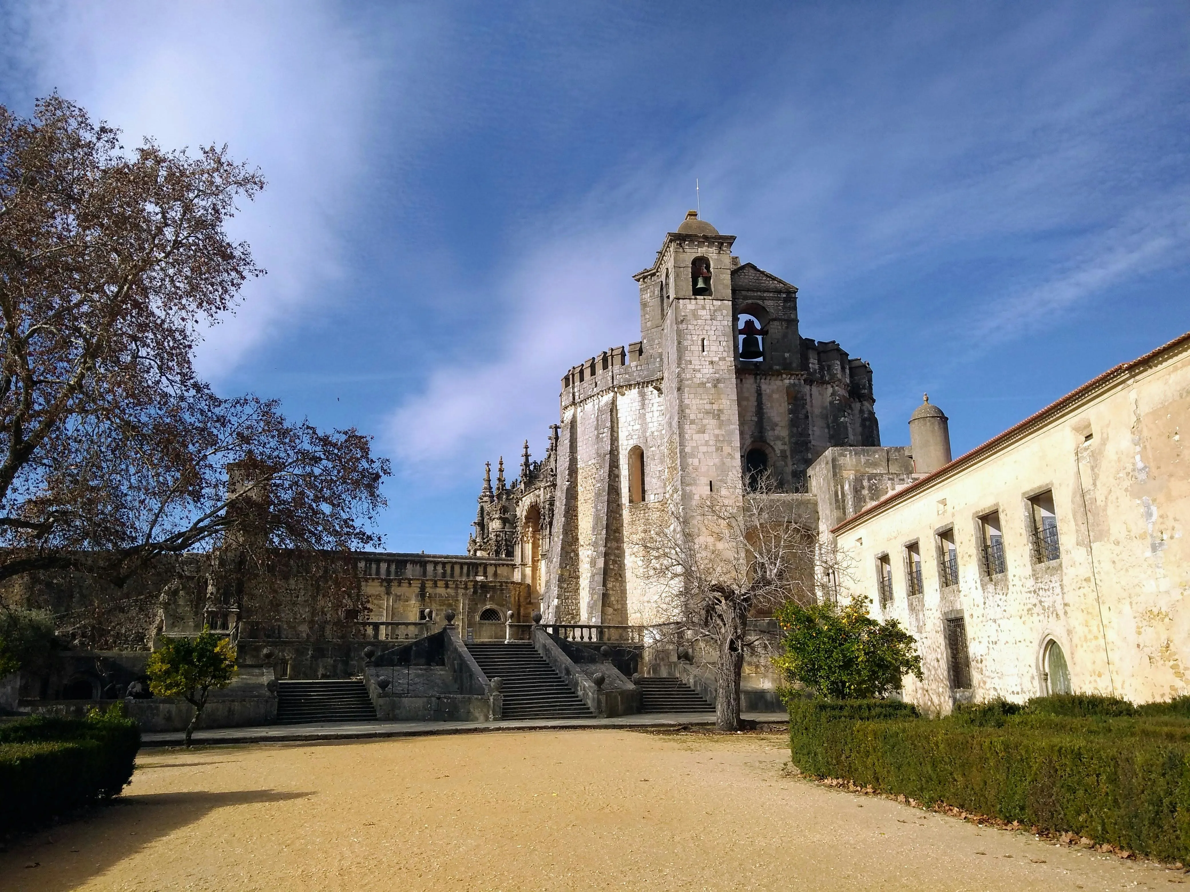 Ornate Manueline window of Tomar Convent of Christ glowing in soft golden morning light with lush greenery