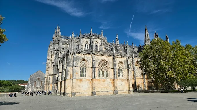 Intricate Gothic limestone facade of Batalha Monastery glowing under soft golden morning light with clear blue sky