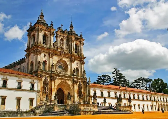 Majestic Gothic facade of Alcobaça Monastery illuminated by warm golden sunset light with lush green gardens