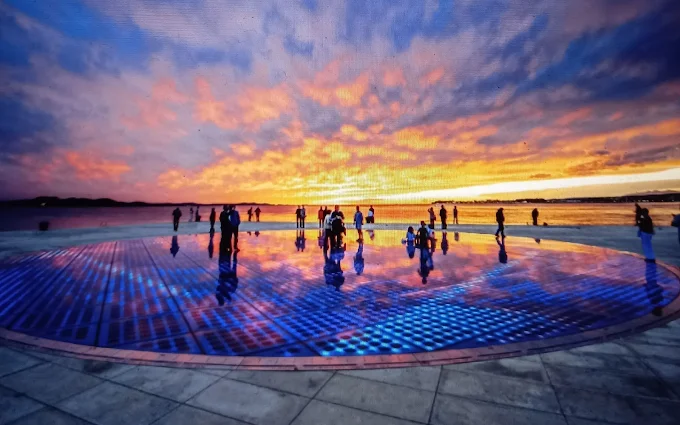 Greeting to the Sun at twilight, Croatia: Circular solar installation glowing with LED lights, soft evening light illuminating the interactive artwork as it responds to the setting sun over the Adriatic