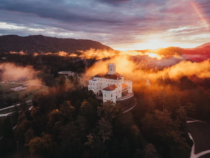 Trakošćan Castle Croatia at golden hour with romantic Gothic Revival architecture, forested hilltop, mirror-like lake reflection, and misty Zagorje countryside