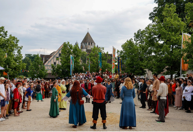 Medieval fair in Provins, France, with costumed performers, colorful market stalls, and the 12th-century Caesar Tower rising in the background under a bright blue sky