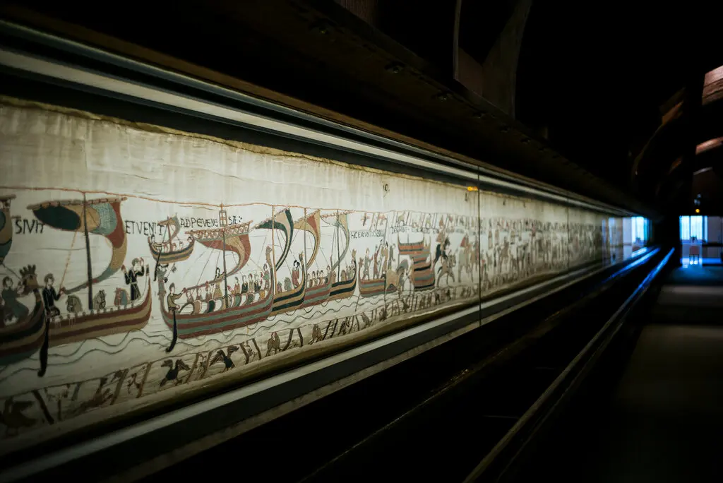 The Bayeux Tapestry displayed in a softly lit gallery at the Musée de la Tapisserie de Bayeux, Normandy, France, its vibrant 11th-century embroidery glowing under museum lighting