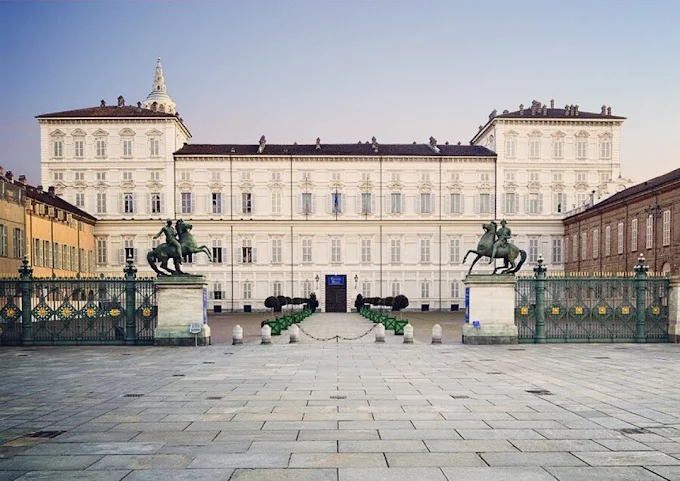 Turin Royal Palace at golden hour, Baroque façade glowing under soft evening light with Piazza Castello bustling below