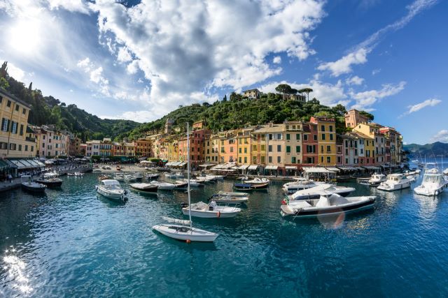 Portofino harbor at golden hour, pastel-colored buildings surrounding a yacht-filled cove with the Ligurian Sea glowing in soft sunset light