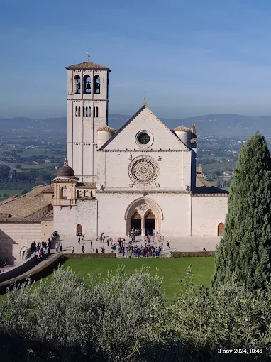 Assisi - Basilica of St. Francis at golden hour, pink stone façade glowing against the Umbrian hills under soft evening light