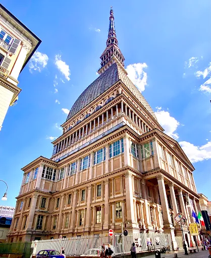 Mole Antonelliana in Turin at golden hour, towering spire glowing against a soft evening sky with city lights below