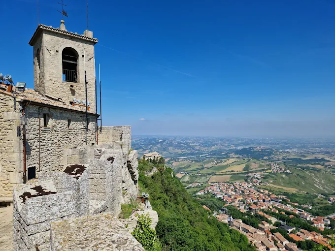 San Marino fortress at golden hour, medieval stone towers and battlements glowing against the Apennine Mountains under soft sunset light