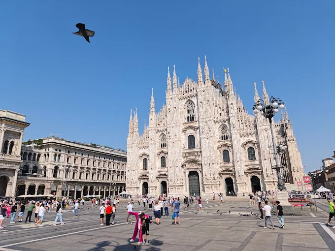 Milan Cathedral (Duomo) at golden hour, intricate Gothic spires glowing against a soft evening sky with Piazza del Duomo bustling below