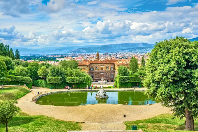 Boboli Gardens in Florence at golden hour, cypress-lined avenues leading to classical fountains and the city skyline beyond