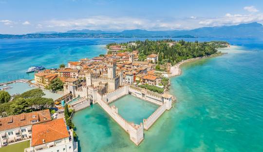 Lake Garda - Sirmione at golden hour, medieval Scaliger Castle and pastel buildings glowing under soft sunset light with lake waters shimmering