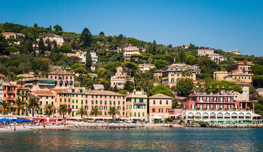 Santa Margherita Ligure at golden hour, pastel buildings lining a calm harbor with fishing boats and palm trees under soft sunset light