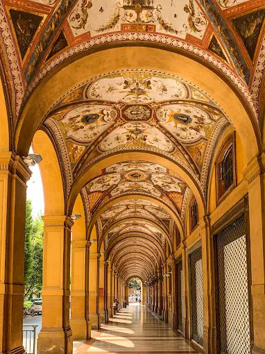 Bologna porticoes at golden hour, long arched colonnades stretching through historic streets with warm light filtering through terracotta rooftops
