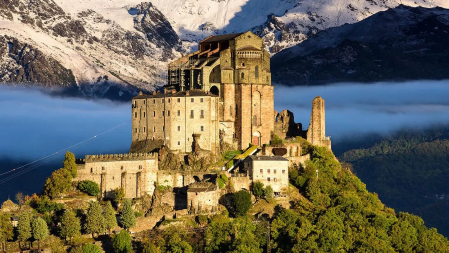 Sacra di San Michele at sunrise, medieval abbey perched on Mount Pirchiriano with mist swirling in the Susa Valley below