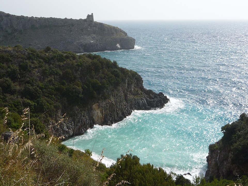 Turquoise waters of the Cilento coast meeting dramatic limestone cliffs and a secluded sandy beach under a clear mid-morning sky