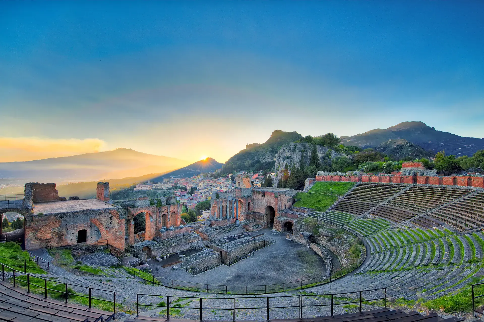 Ancient Greek theater of Taormina with Mount Etna rising in the background, dramatic stone seats, and the Ionian Sea under a clear mid-morning sky