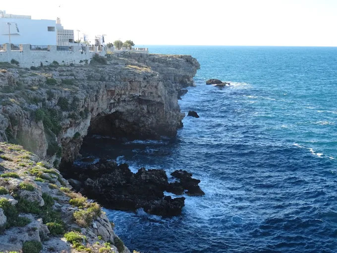 Turquoise waters inside a dramatic sea cave near Polignano a Mare, with sunlight streaming through the entrance and limestone walls at mid-morning