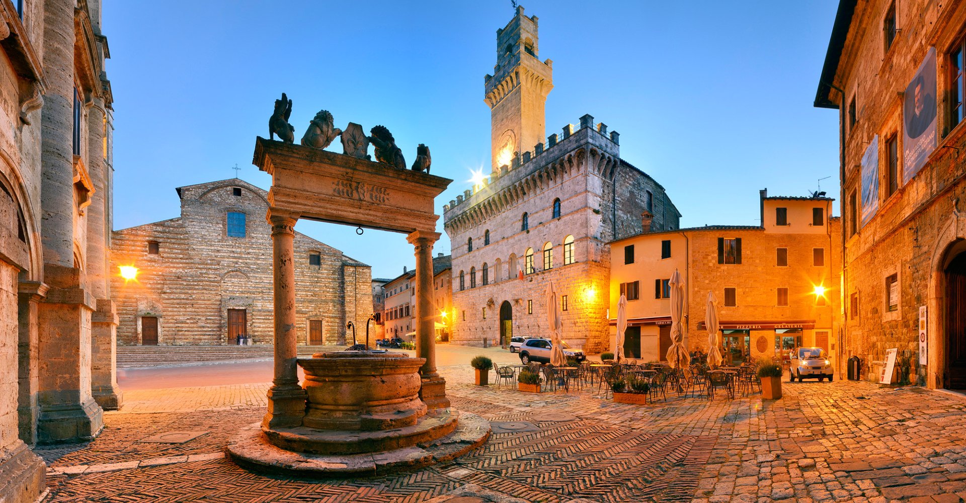 Montepulciano hilltop town at golden hour, terracotta rooftops and Renaissance palaces glowing under soft sunset light with vineyards stretching across the Val d’Orcia