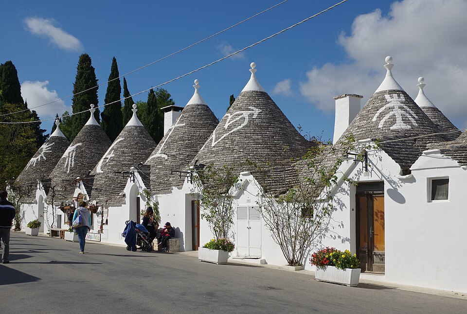 Sun-drenched Alberobello trulli houses with conical limestone roofs lining a narrow cobbled street in Puglia, Italy, at mid-morning