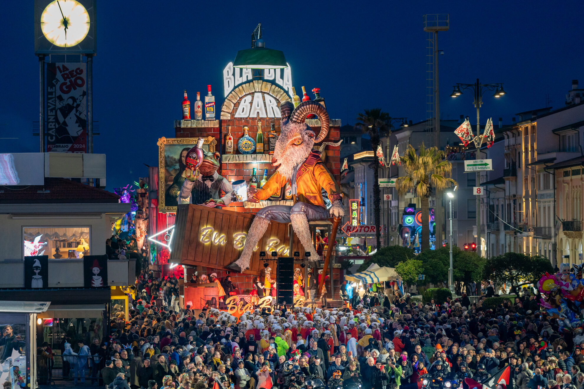 Giant satirical papier-mâché float parading along Viareggio's seafront promenade at dusk during carnival, with crowds and palm trees