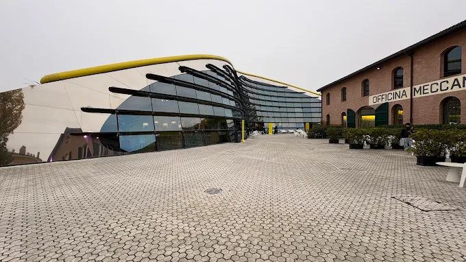 Modena Ferrari museum at golden hour, iconic red F1 cars glowing under soft sunset light in the Enzo Ferrari Museum courtyard