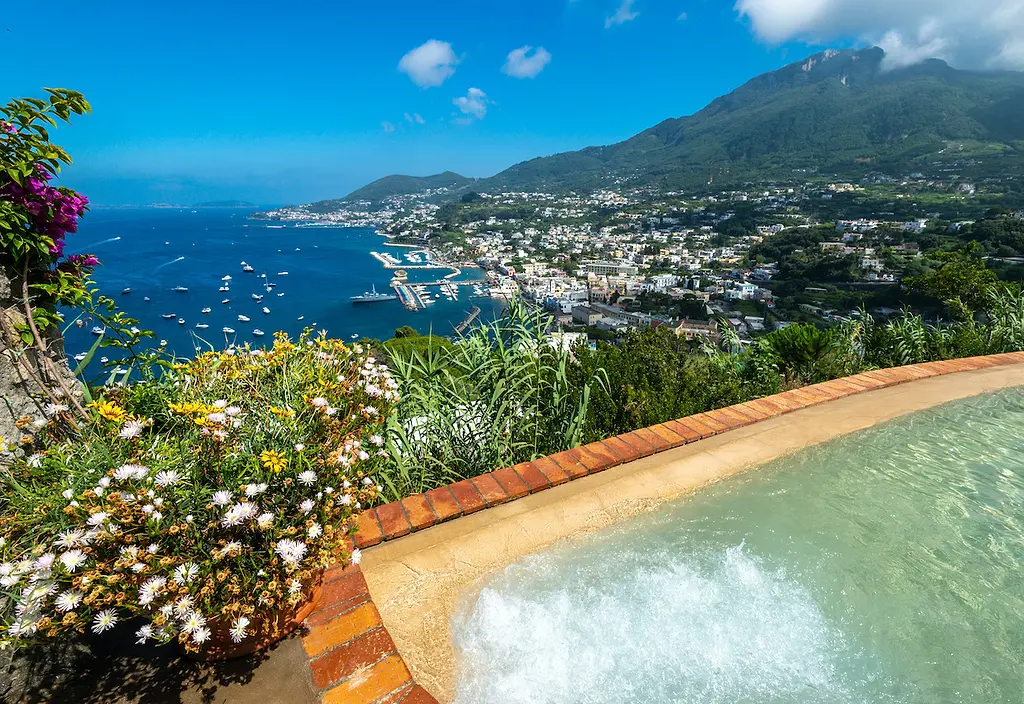 Steam rising from a natural thermal pool in Ischia, surrounded by lush Mediterranean gardens and volcanic rock at mid-morning