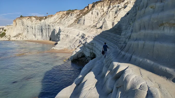 The dramatic white cliffs of Scala dei Turchi with smooth, wave-carved steps leading into the turquoise Mediterranean Sea under a clear mid-morning sky