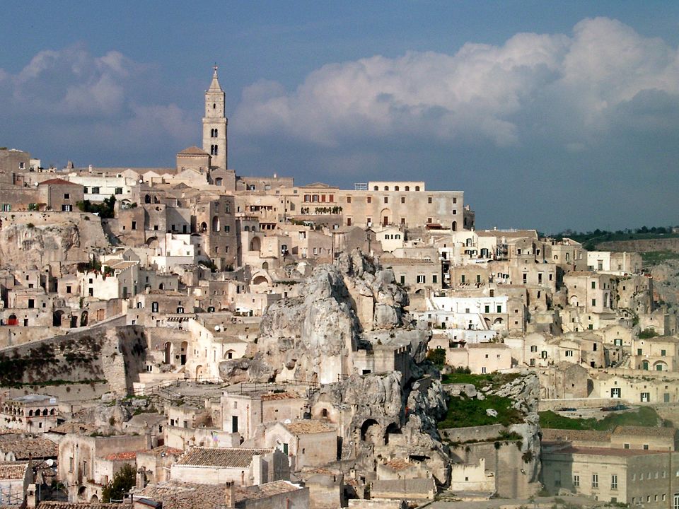 Sunset over Matera's Sassi cave dwellings, with honey-colored stone houses cascading down a ravine and the deep gorge of Gravina in the background