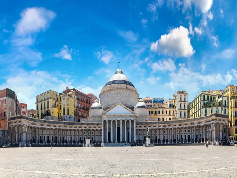 Sun-drenched Spaccanapoli street in Naples historic center, with laundry lines, Baroque facades, and vibrant street life under a clear blue sky at mid-morning