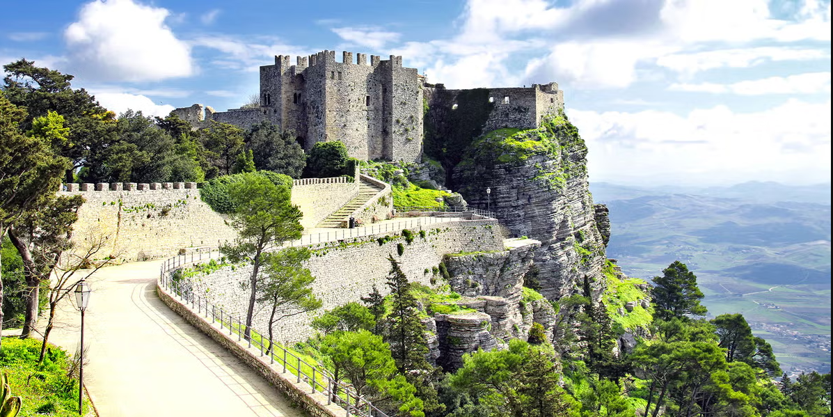 Sun-drenched medieval hilltop town of Erice with stone walls, terracotta roofs, and panoramic views of Sicily under a clear mid-morning sky