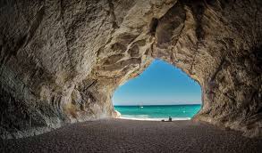 Turquoise waters of Cala Luna beach framed by dramatic white limestone cliffs and sea caves in Sardinia at mid-morning