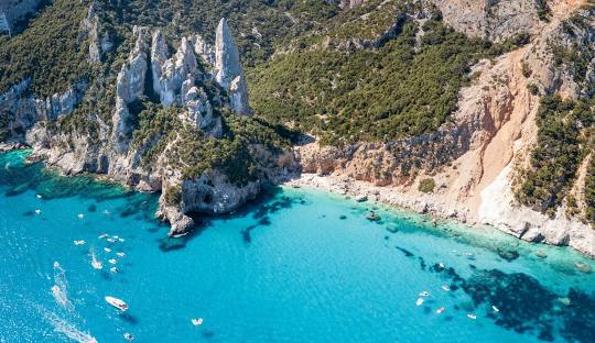 Turquoise waters of Gulf of Orosei meeting white limestone cliffs at Cala Luna beach in Sardinia during mid-morning light