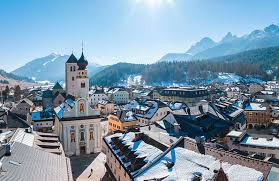 Sunrise over San Candido-Innichen in South Tyrol, golden light illuminating alpine meadows with traditional villages and Dolomite peaks at dawn