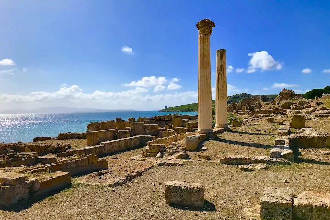 Sunset over Tharros archaeological site on Sardinia's Sinis Peninsula, golden light illuminating Phoenician ruins against turquoise Mediterranean waters at dusk