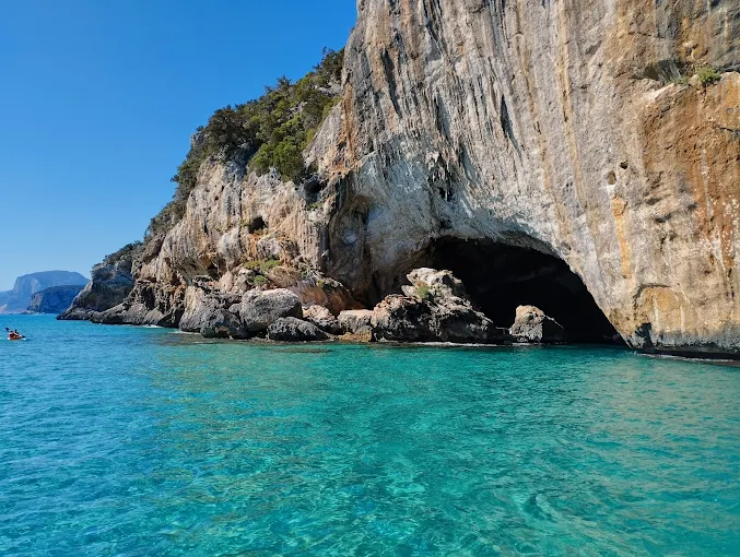 Sunlight piercing through the entrance of Grotta del Bue Marino sea cave in Sardinia's Gulf of Orosei at mid-morning, illuminating turquoise waters and limestone formations