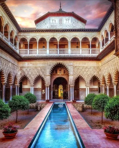 Real Alcázar palace gardens at sunrise with intricate Moorish arches, reflective pools, and lush greenery bathed in soft Andalusian morning light