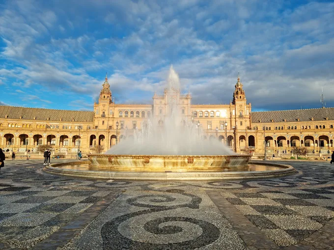 Plaza de España Seville semi-circular brick building with tiled benches and canal reflecting blue sky and white clouds during midday