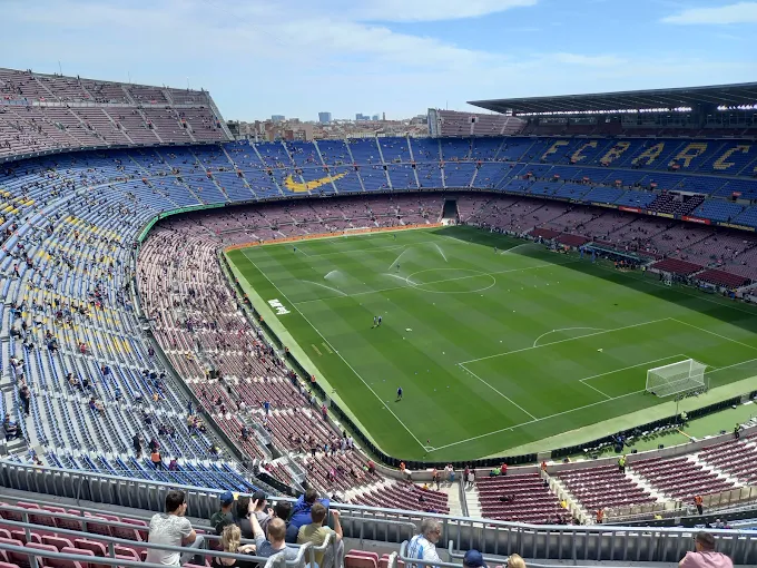 Camp Nou stadium at sunset with golden light illuminating the iconic stands and FC Barcelona crest glowing against Barcelona skyline