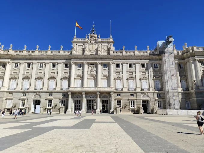 Royal Palace Madrid grand stone facade at sunset with manicured gardens and blue sky bathed in warm Castilian evening light