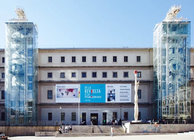 Reina Sofia Museum Madrid modern glass facade at sunset with visitors and sculptures bathed in warm evening light